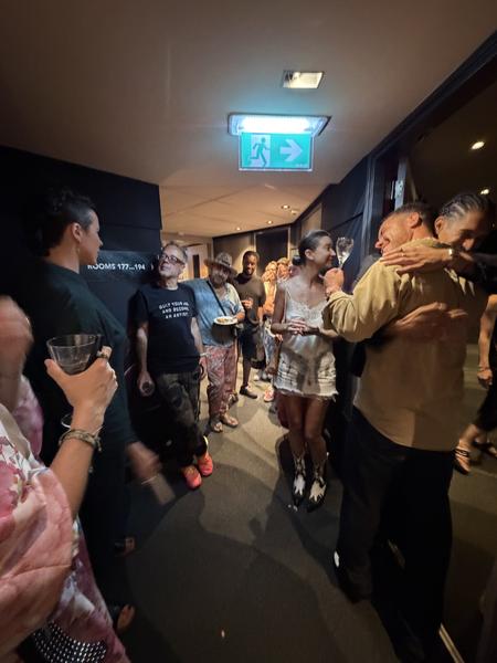This lively indoor photo captures a group of people socializing and enjoying drinks in a dimly lit corridor, likely at a hotel or event space on Amstelstraat, Centrum, Amsterdam